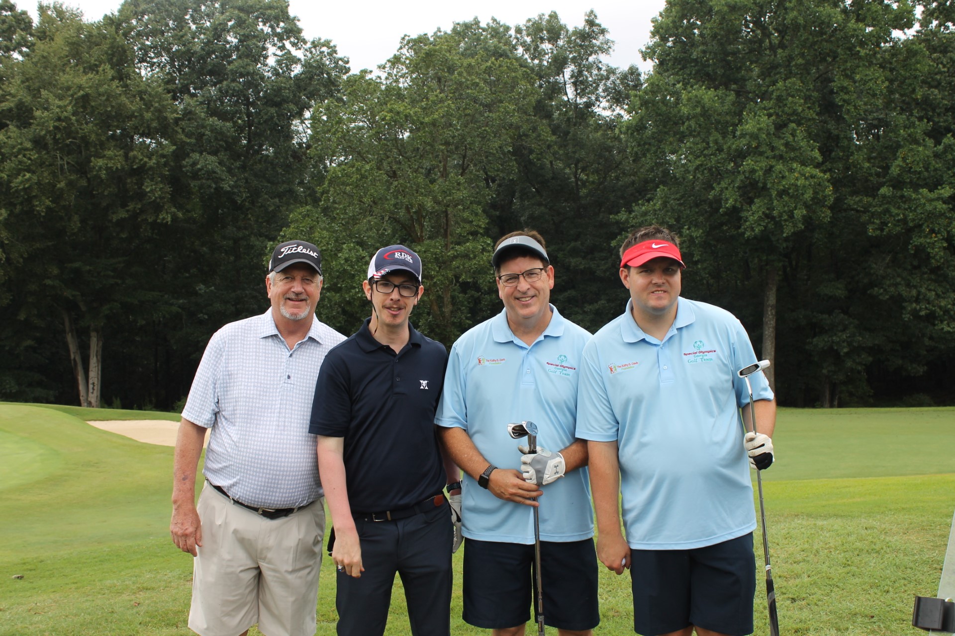 A photograph of four men standing on the golf green and smiling at the camera.